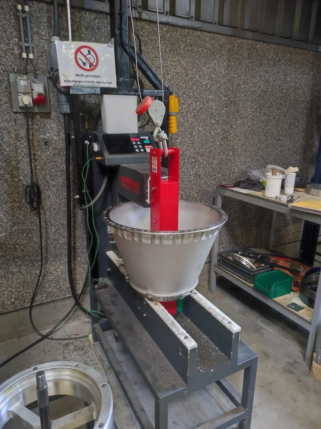 Industrielle Waage mit großem weißem Behälter auf rotem Ständer in Werkstatt, Warnsschild oben sichtbar.