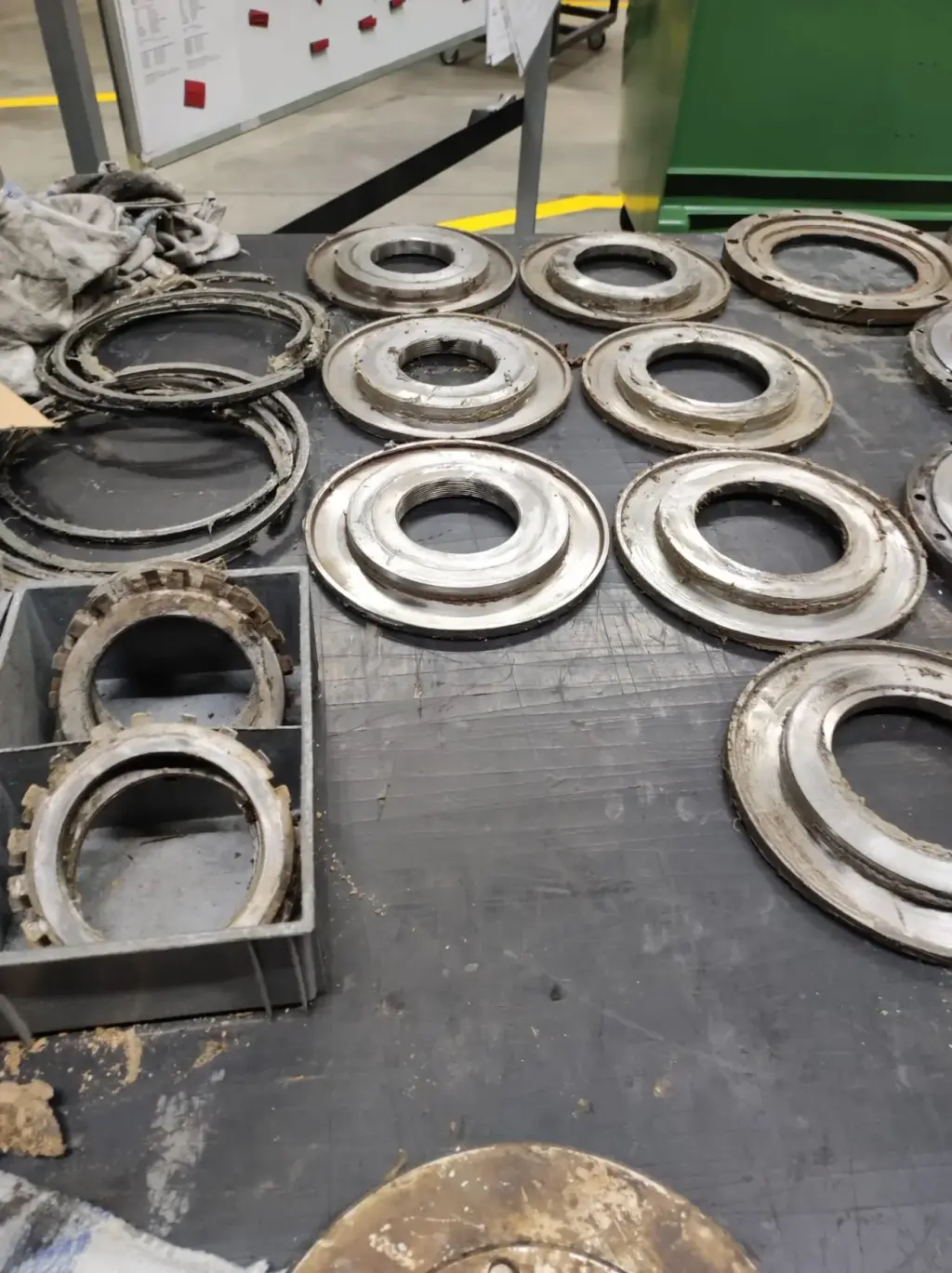 Mehrere abgenutzte Metallringe und Dichtungen auf dunklem Werkbänktisch in Industriewerkstatt ausgelegt.
